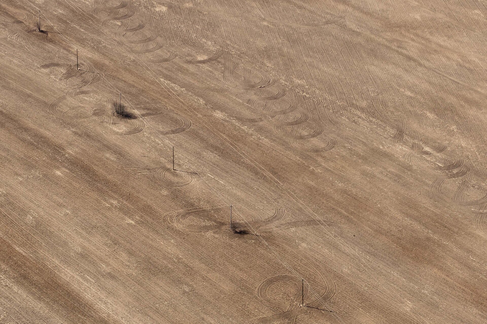 An aerial view of a dry field with tire marks across it in the dirt. Image credit: Vladimir Chuchadeev